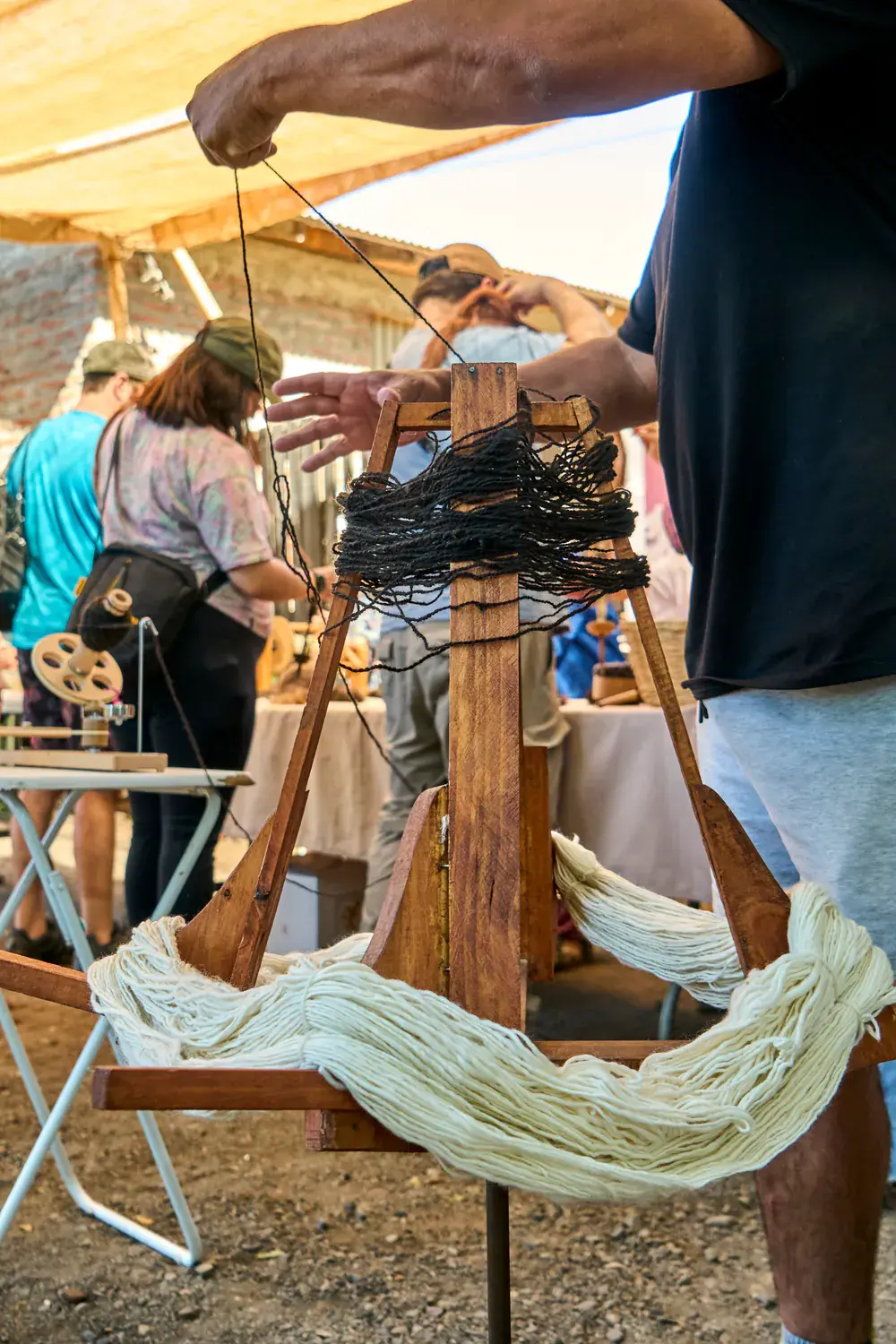 A participant winds a skein of white wool on a wooden swift