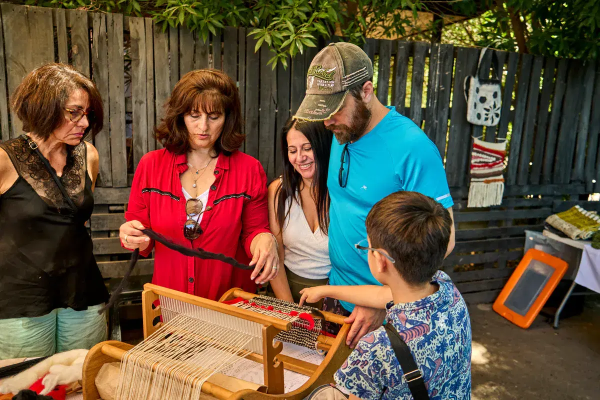 A family and the artisan look at a small loom with black wool