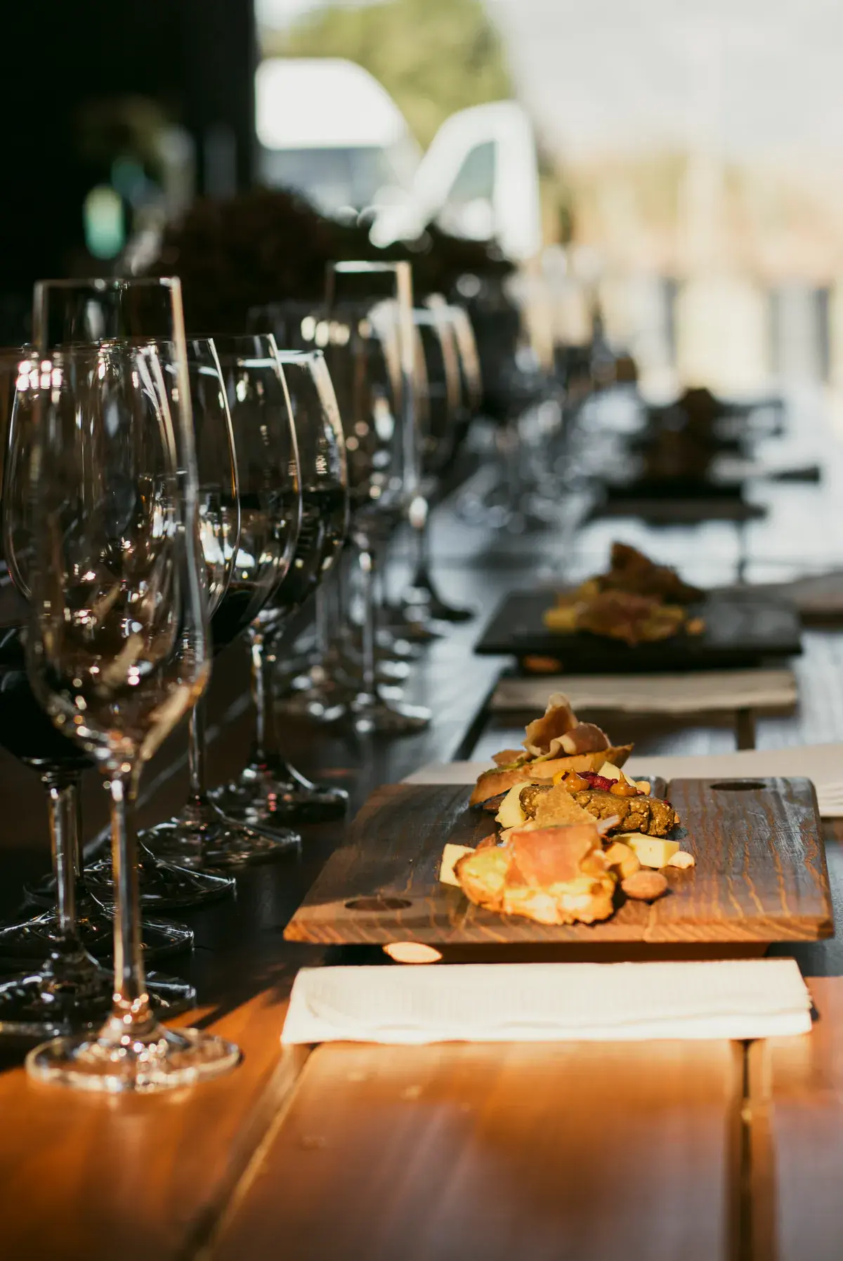 Glasses lined up and a board of bites on the tasting table, in the light from the window