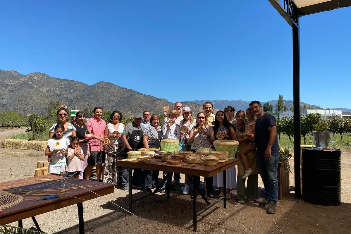 Group photo of the participants with their finished wicker pieces, with the mountains behind