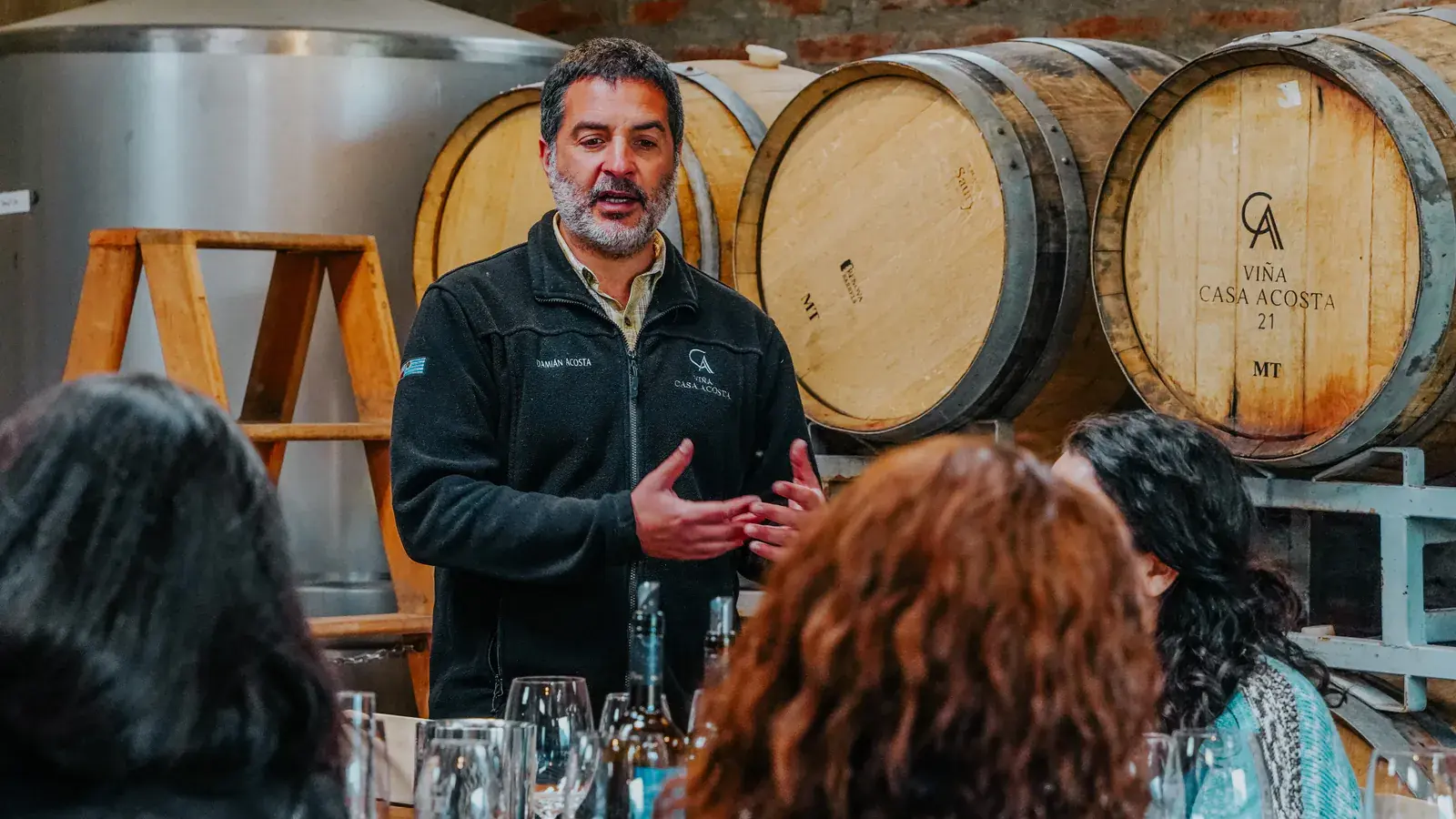 The host presents the wines to a group seated before their glasses, in the barrel room