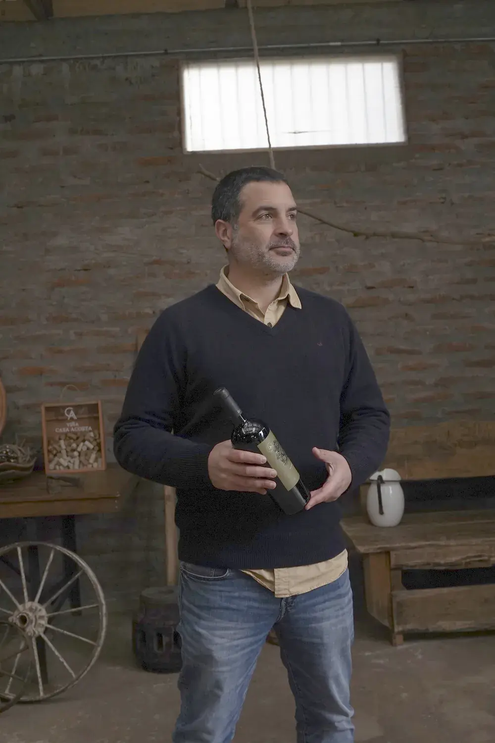 The host holds a bottle in the cellar, among Viña Casa Acosta signs