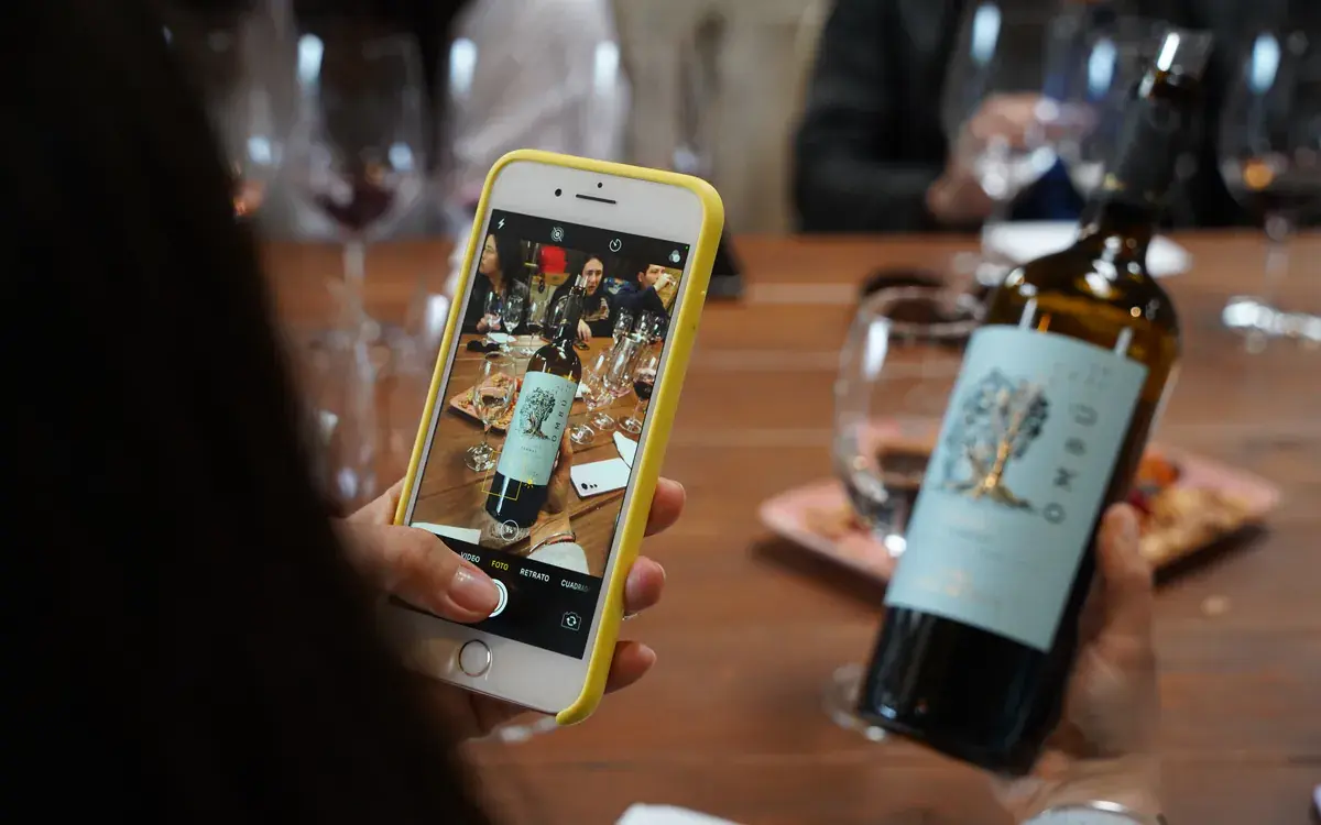 A visitor photographs a bottle of Ombú with a phone on the tasting table