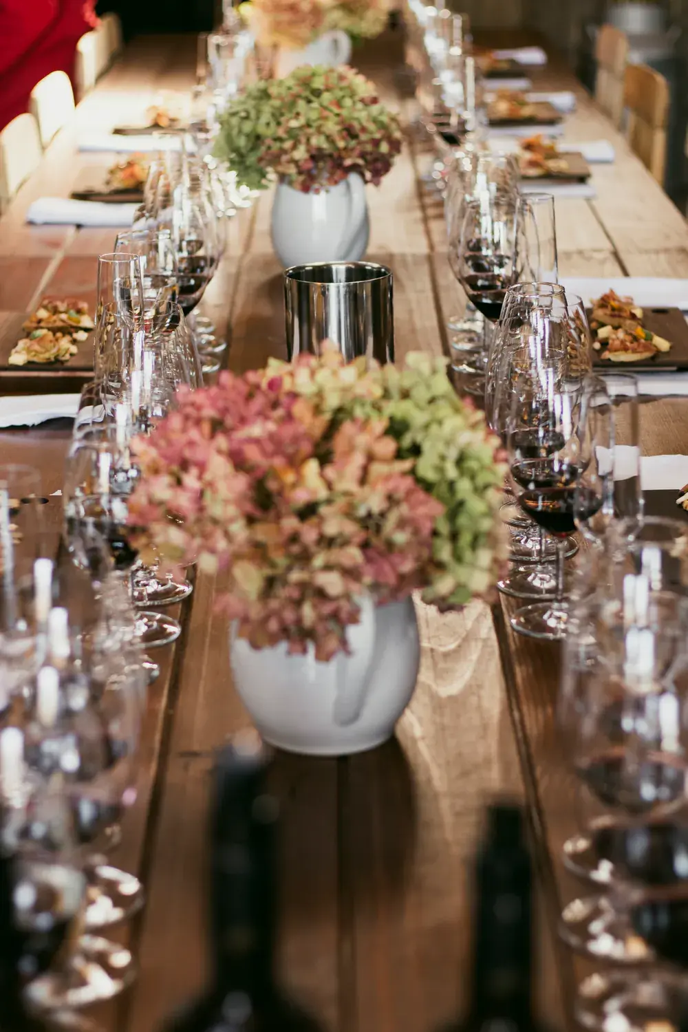 A long table set for the tasting, with glasses in a row, boards of bites and hydrangeas