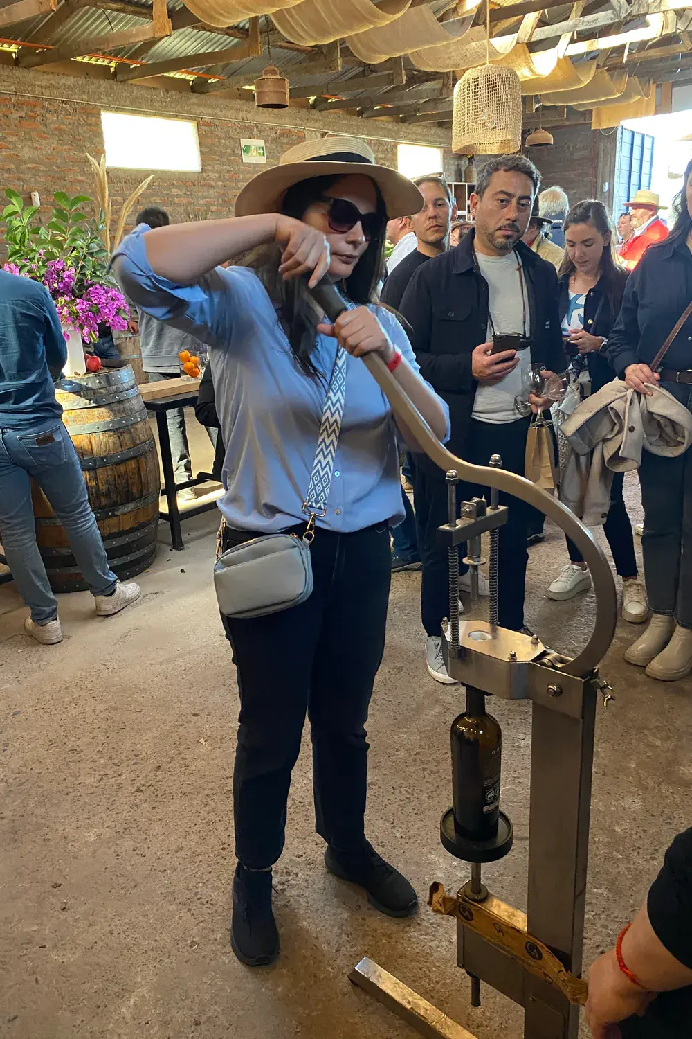 A visitor corks a bottle with a hand corker while the group looks on