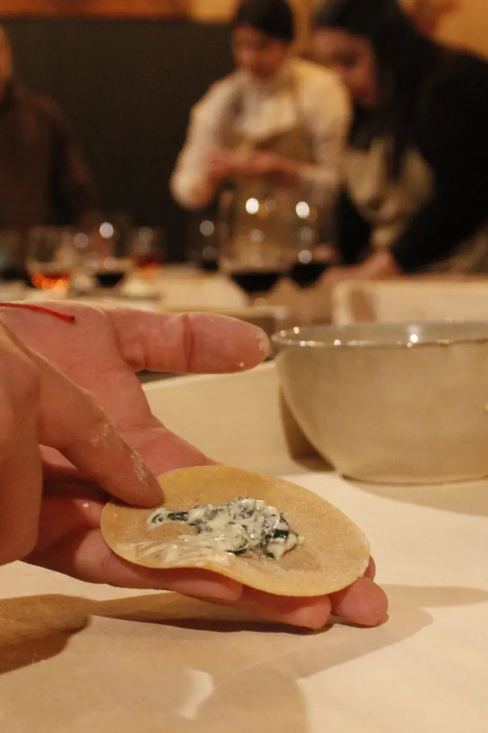 A hand holds a disc of dough with its filling before closing it