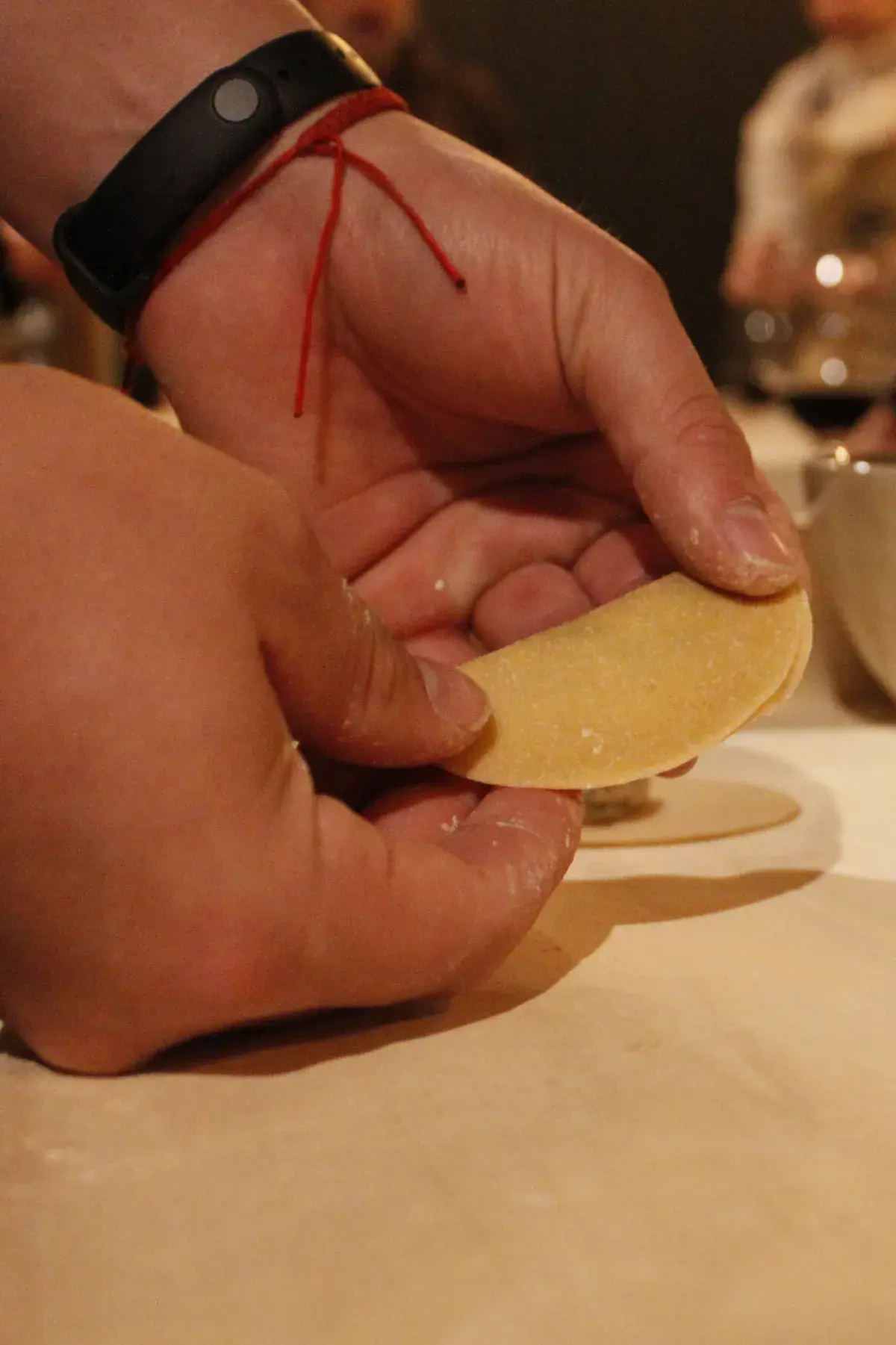 Floury hands fold the filled disc to shape the pasta