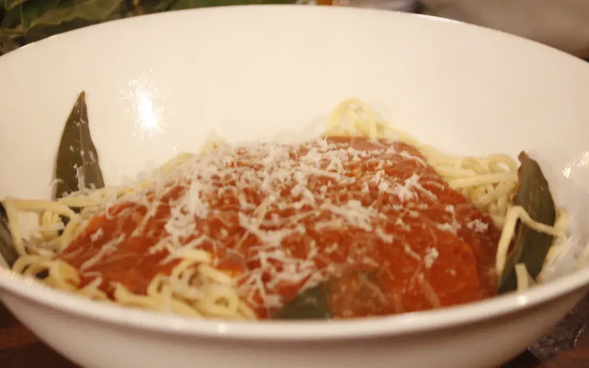 A plate of fresh pasta with tomato sauce, grated cheese and bay leaves