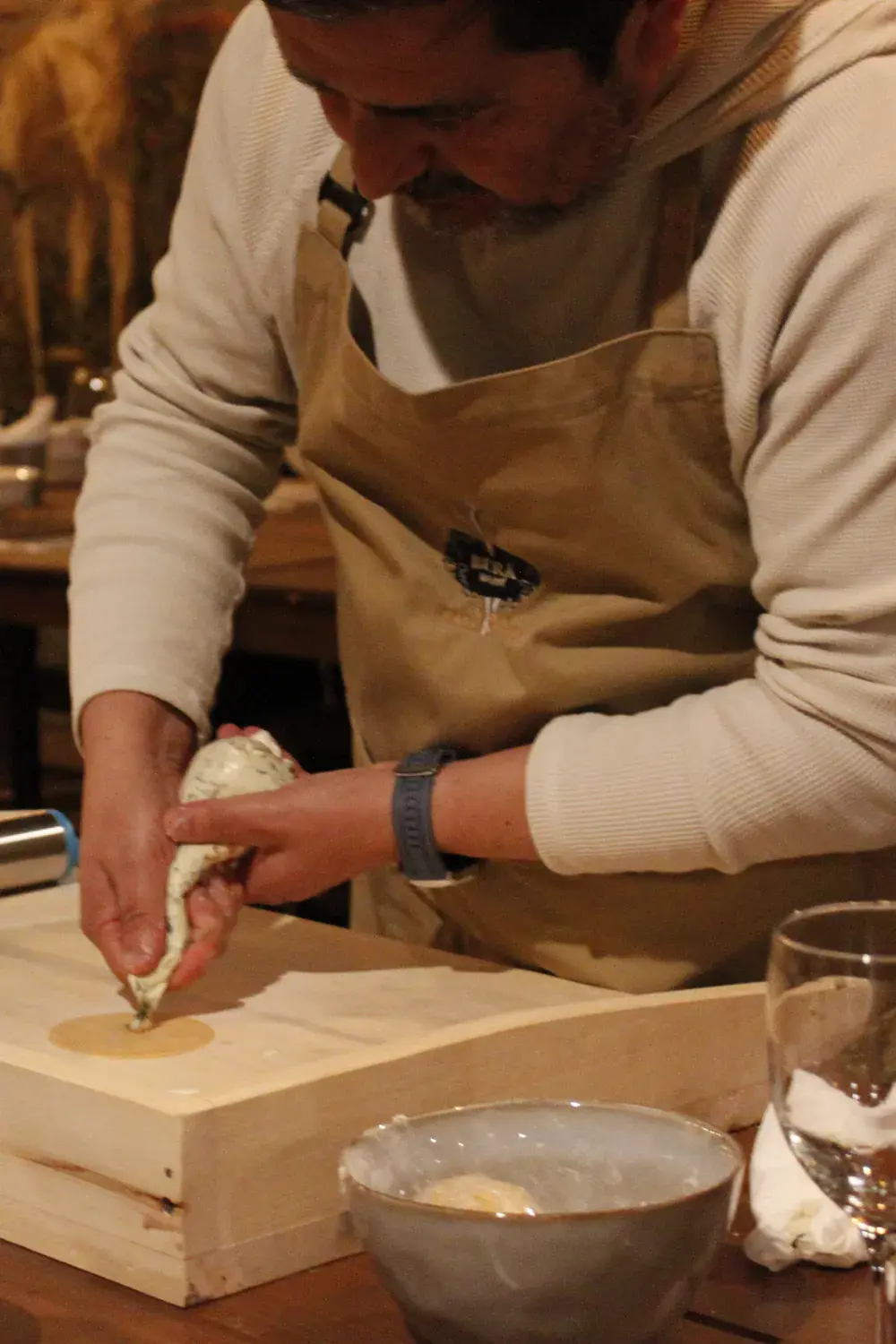 A participant in an apron pipes filling onto a disc of dough, beside glasses of wine