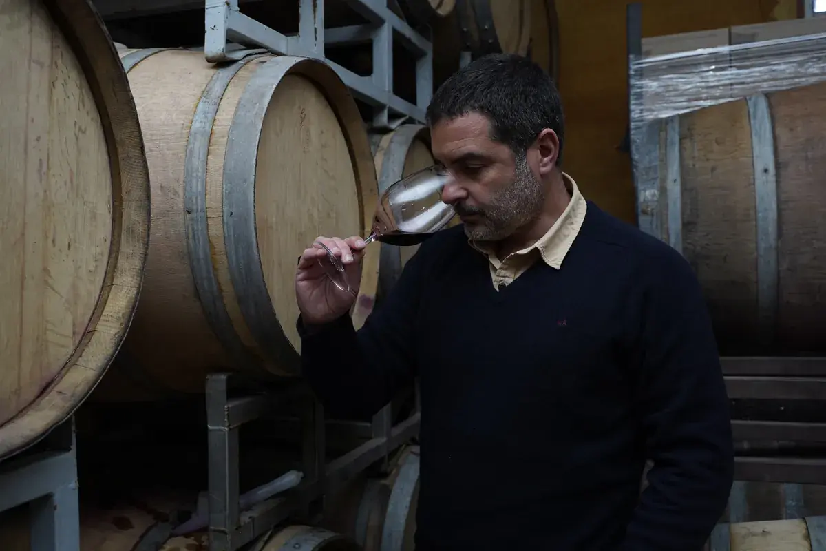 The host noses a glass of red wine among the barrels