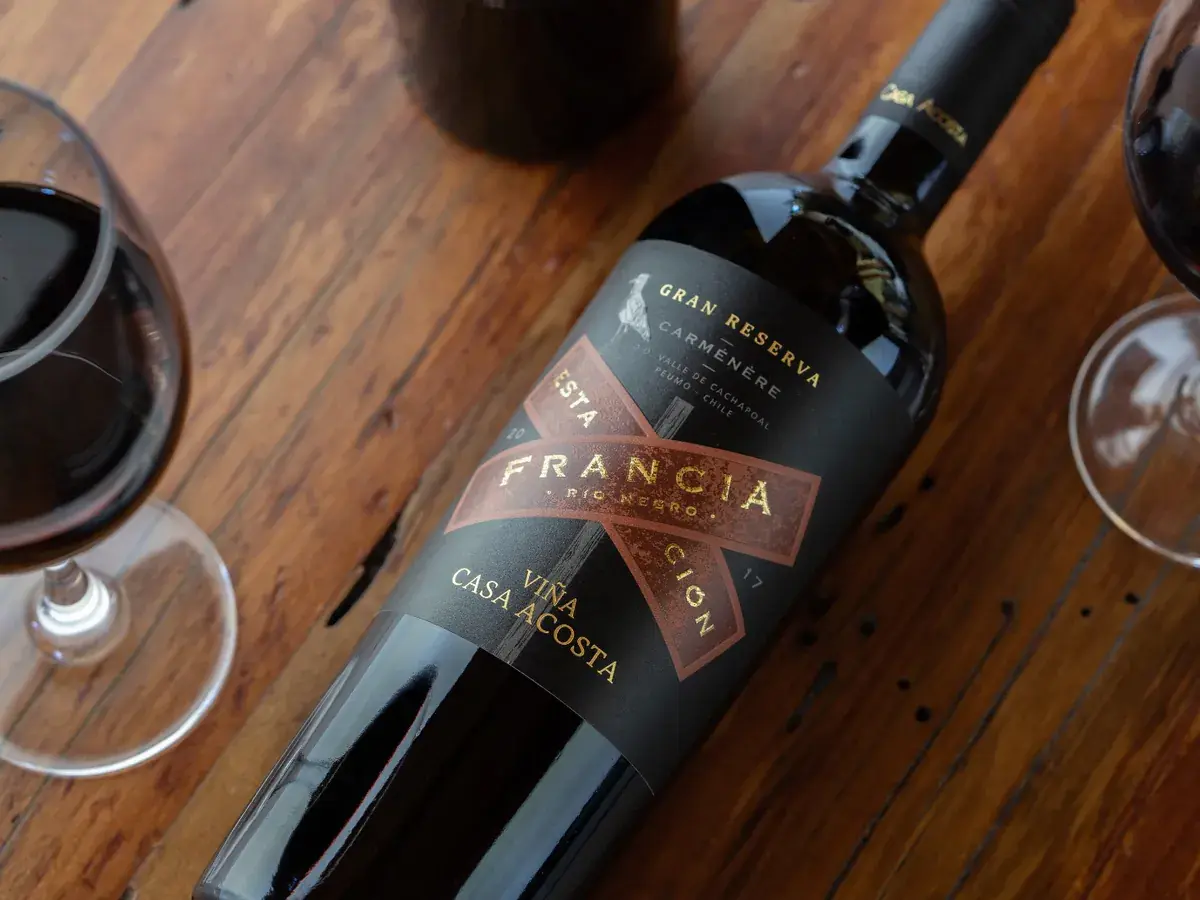 A bottle of Estación Francia Gran Reserva Carménère 2017 beside two glasses of red wine