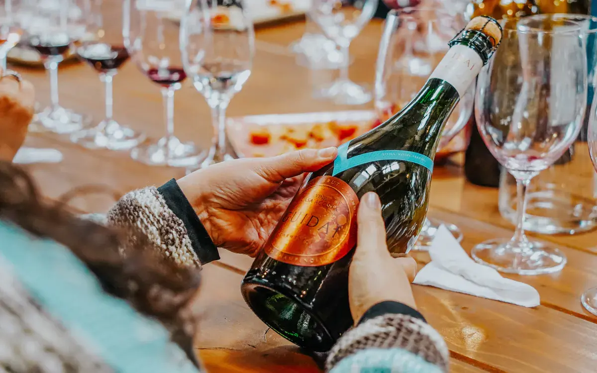 Hands hold a bottle of Guidaí sparkling wine over the tasting table