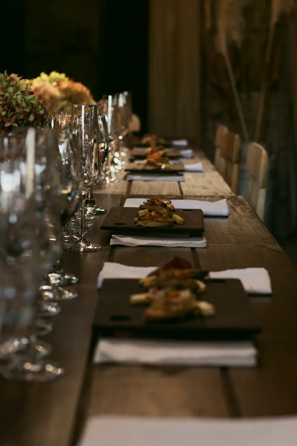A long tasting table with boards of bites, glasses and hydrangeas, in low light