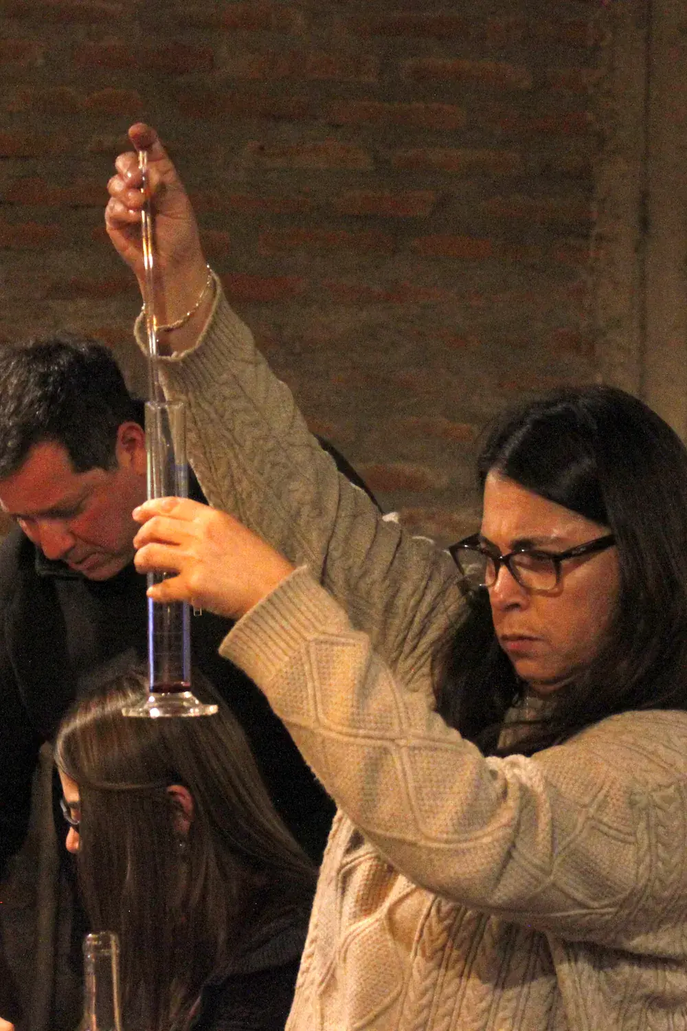 A participant lifts a cylinder of wine while measuring a blend