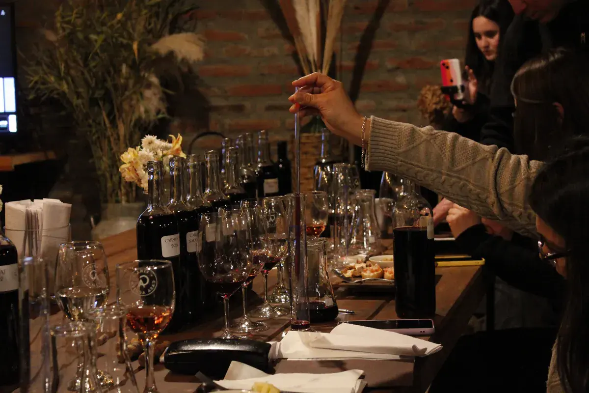 A participant stirs the wine in the cylinder with a rod, among labelled bottles