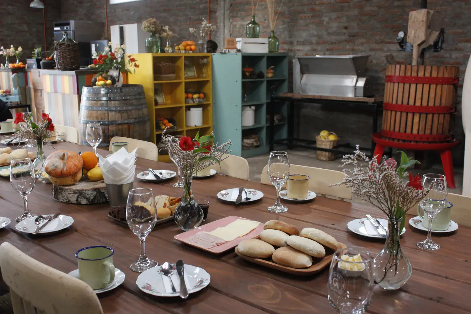 Mesa larga puesta para el desayuno campesino, con panes, copas y flores del campo