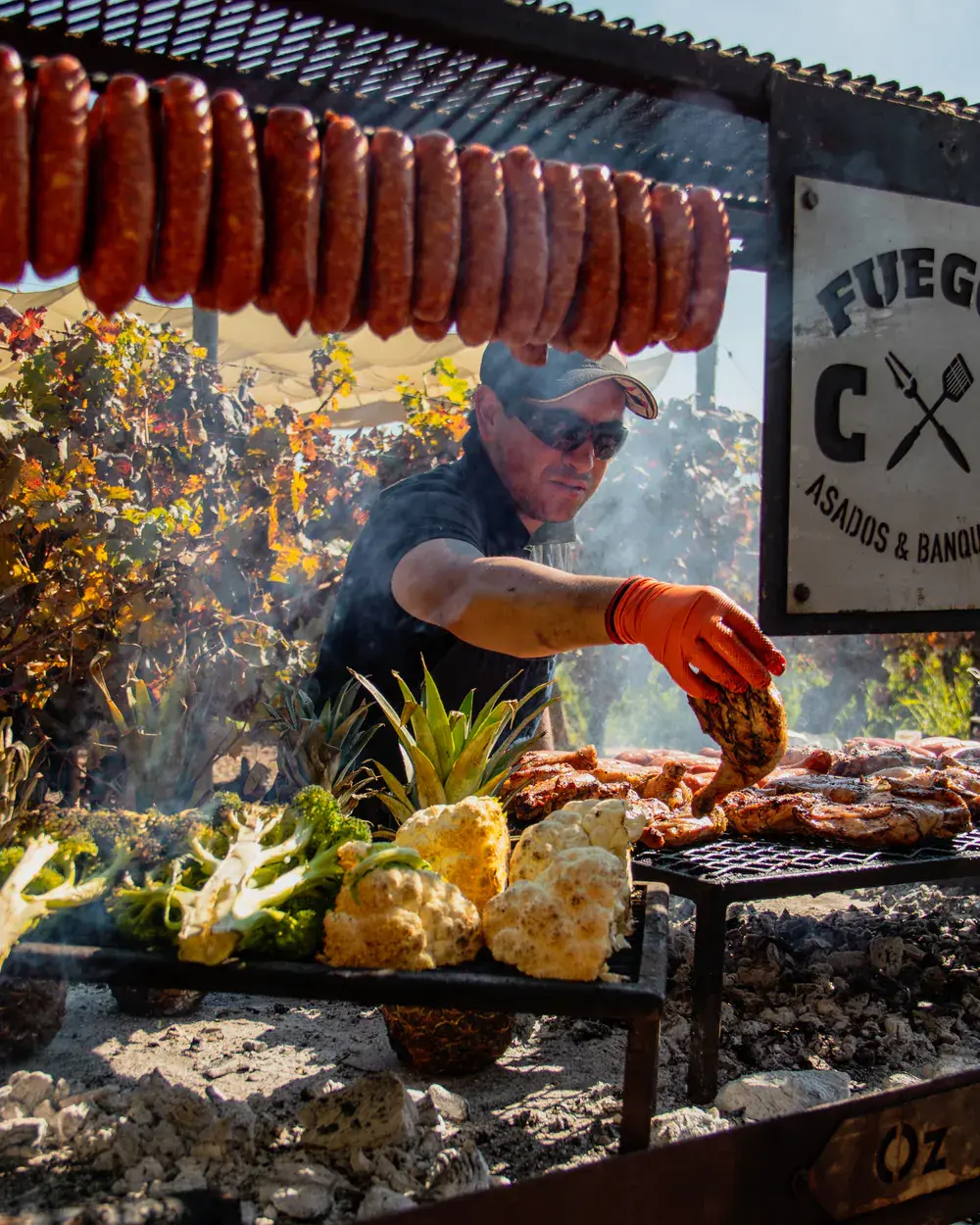 The grill master turning the meat on the grill, beneath a row of hanging chorizos