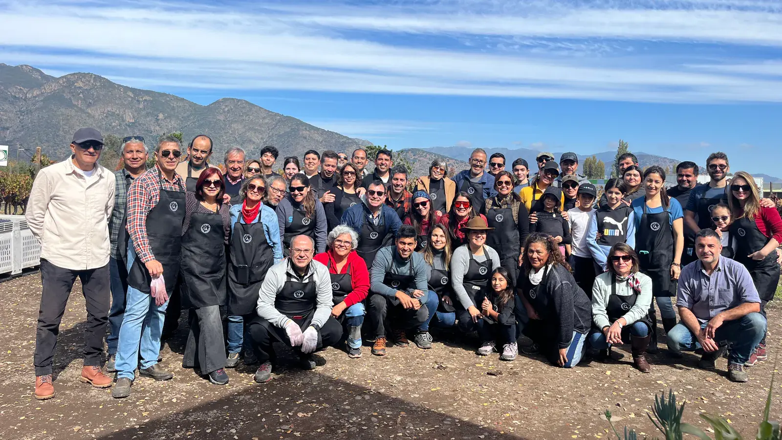 Group photo of the harvest guests in aprons, with the mountains behind