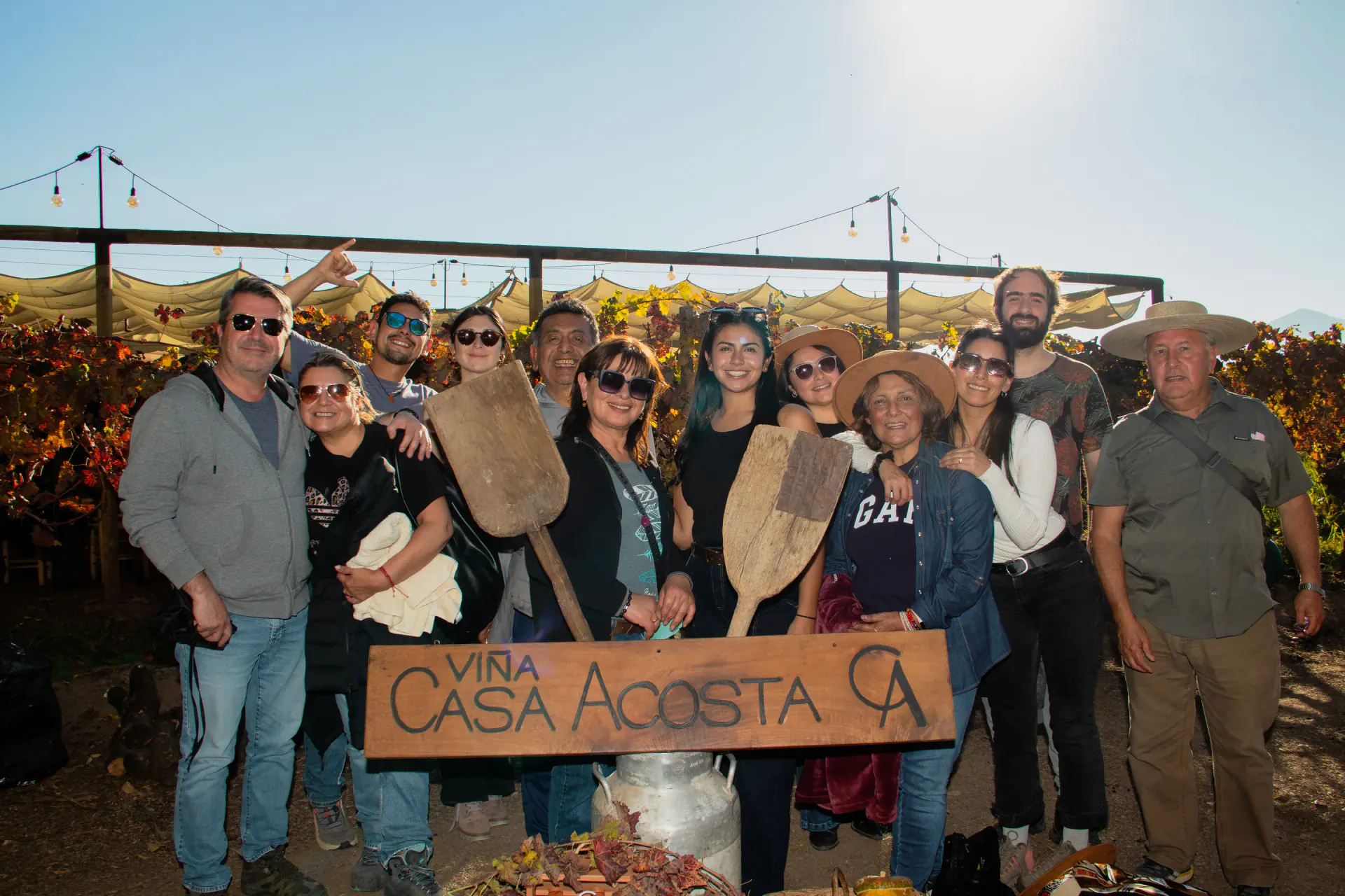 Grupo de visitantes posando con el cartel tallado de Viña Casa Acosta entre las parras del viñedo en otoño, a contraluz del atardecer